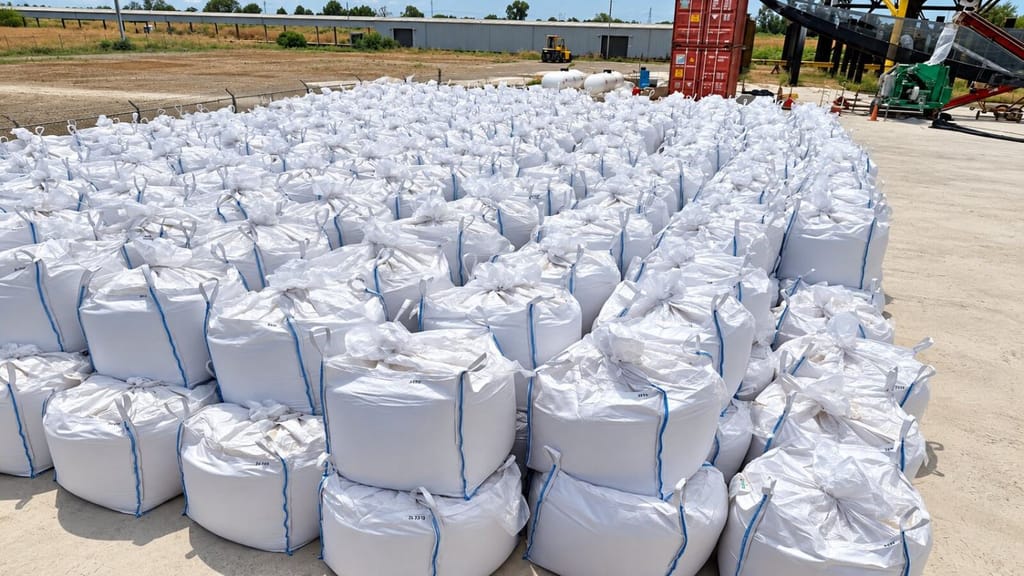 Rows of filled white bulk bags of aragonite staged in an outdoor yard